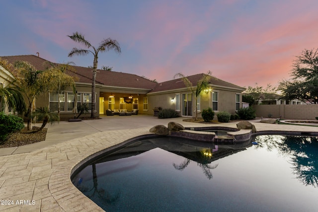 pool at dusk featuring an in ground hot tub and a patio