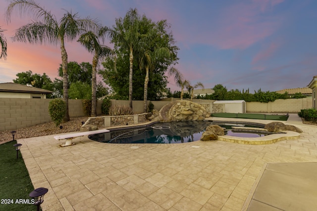 pool at dusk featuring a patio, a diving board, and an in ground hot tub