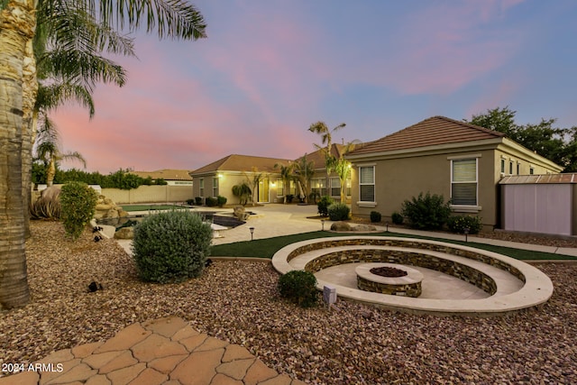 back house at dusk with an outdoor fire pit, a shed, and a patio area