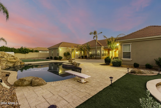 pool at dusk featuring a patio and a diving board