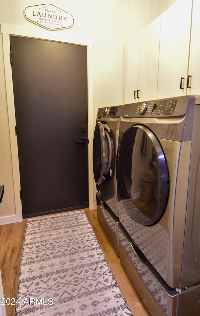 clothes washing area featuring cabinets, light wood-type flooring, and washing machine and dryer