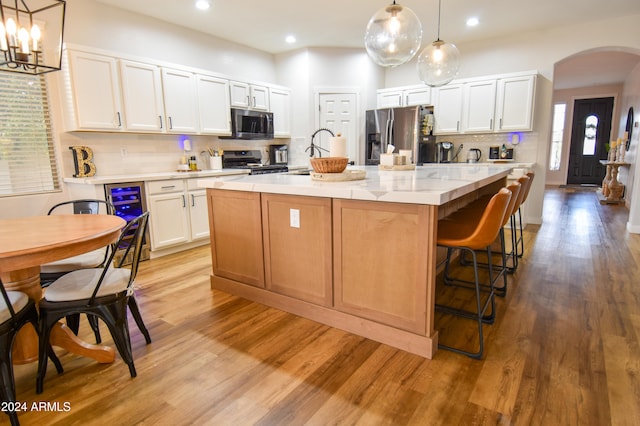 kitchen with appliances with stainless steel finishes, a kitchen island with sink, pendant lighting, light hardwood / wood-style flooring, and white cabinets