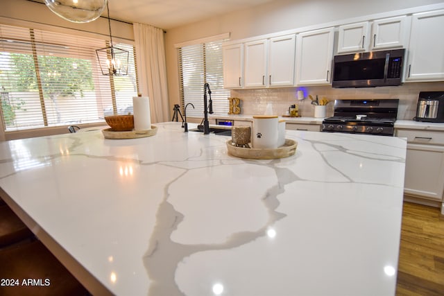 kitchen with white cabinetry, hanging light fixtures, stainless steel appliances, dark hardwood / wood-style floors, and a center island with sink