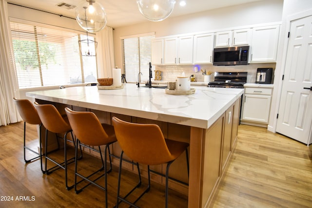 kitchen with a center island with sink, white cabinetry, hanging light fixtures, and appliances with stainless steel finishes