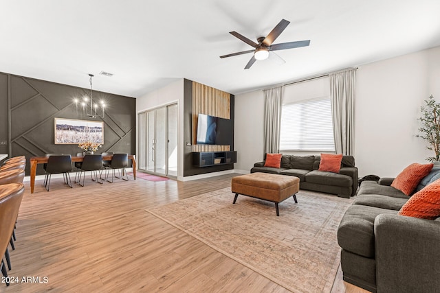 living room with ceiling fan with notable chandelier and light hardwood / wood-style floors