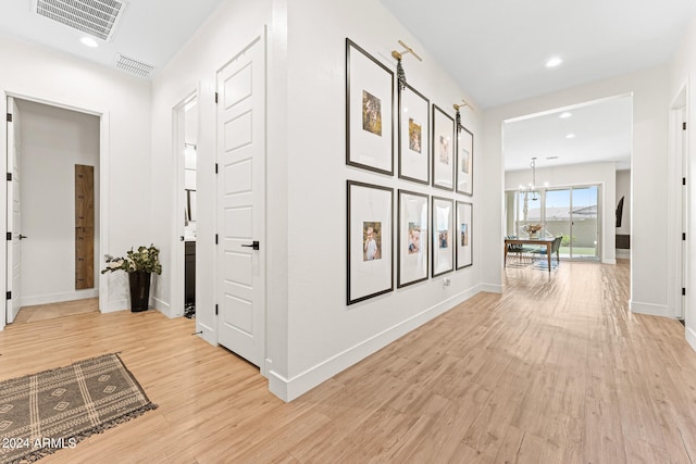 corridor featuring light wood-type flooring and a notable chandelier