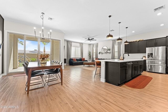 kitchen with stainless steel appliances, light hardwood / wood-style floors, hanging light fixtures, and a kitchen island with sink