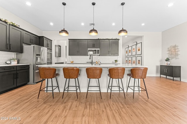 kitchen with an island with sink, stainless steel appliances, and hanging light fixtures