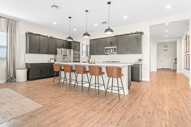 kitchen with decorative light fixtures, a kitchen island with sink, stainless steel appliances, a breakfast bar area, and light wood-type flooring