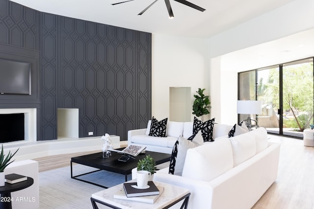 living room with wallpapered walls, wood finished floors, ceiling fan, and an accent wall