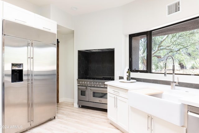 kitchen with high end appliances, sink, light hardwood / wood-style flooring, and white cabinetry