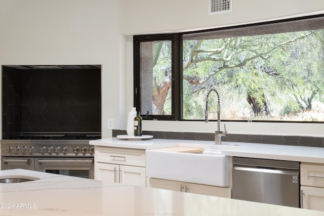 room details featuring light stone counters, stainless steel appliances, white cabinetry, and sink