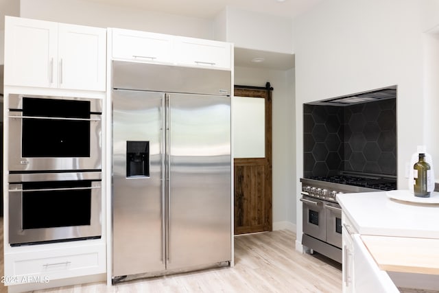 kitchen featuring high end appliances, a barn door, light wood-type flooring, and white cabinetry