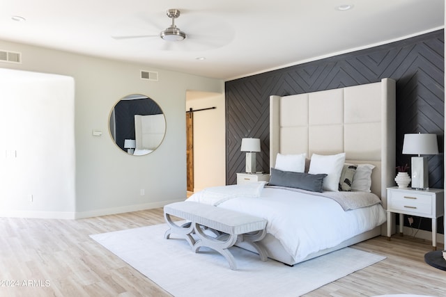 bedroom with light hardwood / wood-style flooring, ceiling fan, and a barn door