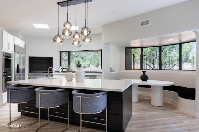 kitchen with light stone counters, white cabinetry, a large island, stainless steel appliances, and visible vents