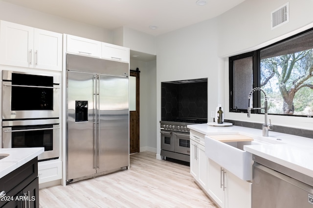 kitchen featuring light wood-type flooring, white cabinetry, sink, a barn door, and premium appliances