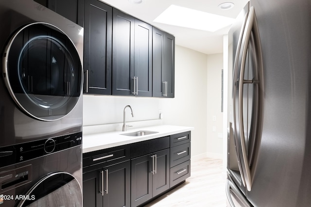 washroom featuring a sink, stacked washer / dryer, baseboards, light wood-style floors, and cabinet space