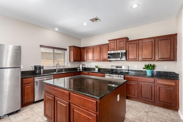 kitchen with stainless steel appliances, a sink, visible vents, a center island, and dark stone countertops