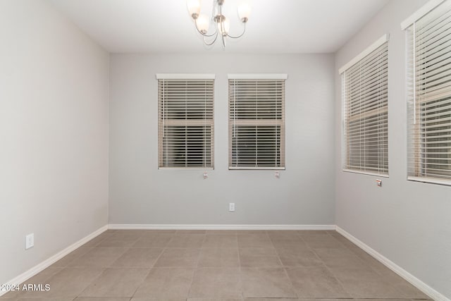 tiled spare room featuring a chandelier