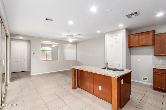 kitchen with ceiling fan, light stone counters, sink, and an island with sink