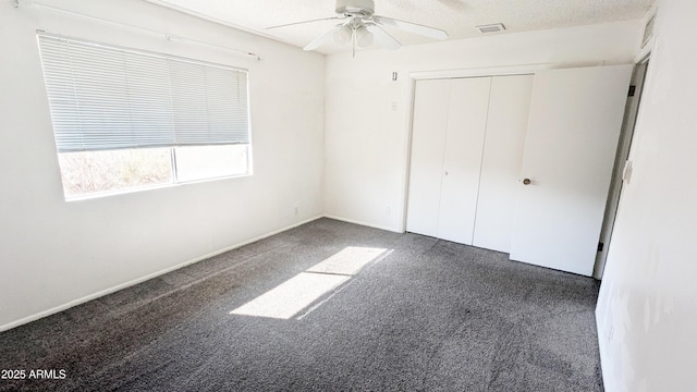 unfurnished bedroom with ceiling fan, a textured ceiling, a closet, and dark colored carpet