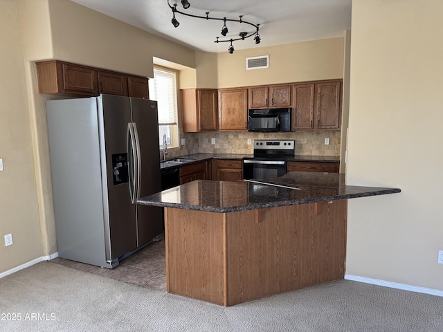 kitchen featuring visible vents, a peninsula, a sink, decorative backsplash, and appliances with stainless steel finishes