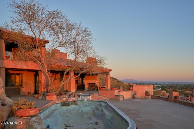 pool at dusk featuring an in ground hot tub, a patio area, and an outdoor fireplace