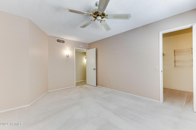 unfurnished bedroom featuring a textured ceiling, ceiling fan, a spacious closet, and light colored carpet