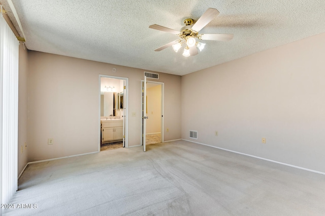 unfurnished bedroom featuring light colored carpet, ceiling fan, connected bathroom, and a textured ceiling