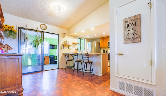 kitchen featuring dark parquet floors, a breakfast bar area, stainless steel fridge, kitchen peninsula, and a textured ceiling