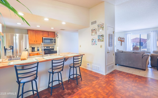 kitchen featuring sink, a breakfast bar, appliances with stainless steel finishes, dark parquet flooring, and a textured ceiling