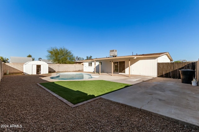 rear view of property featuring cooling unit, a patio, a fenced in pool, a shed, and a lawn