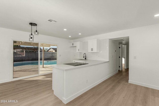 kitchen with kitchen peninsula, sink, pendant lighting, light hardwood / wood-style floors, and white cabinetry