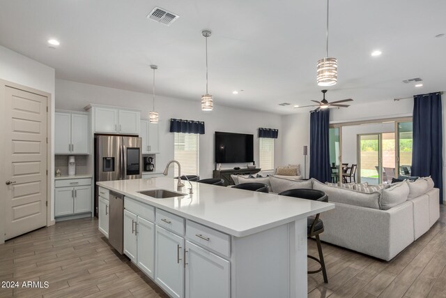 kitchen featuring hanging light fixtures, white cabinets, an island with sink, and appliances with stainless steel finishes