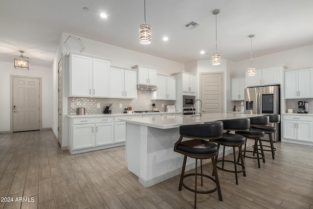 kitchen with white cabinetry, hanging light fixtures, an island with sink, a breakfast bar area, and tasteful backsplash