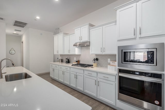 kitchen featuring stainless steel appliances, backsplash, wood-type flooring, white cabinets, and sink