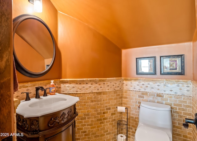 half bath with toilet, a wainscoted wall, lofted ceiling, and vanity