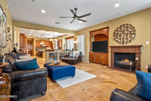 living room featuring ceiling fan with notable chandelier, a glass covered fireplace, visible vents, and recessed lighting