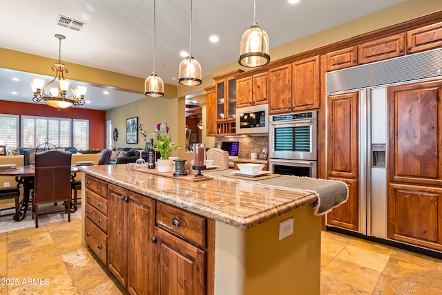 kitchen featuring brown cabinetry, glass insert cabinets, a center island, built in appliances, and pendant lighting