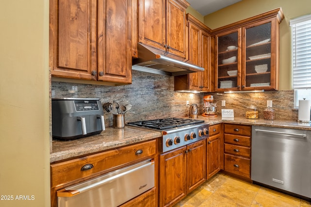 kitchen featuring glass insert cabinets, appliances with stainless steel finishes, light stone counters, under cabinet range hood, and a warming drawer