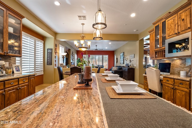 kitchen with visible vents, glass insert cabinets, stainless steel microwave, light stone countertops, and pendant lighting