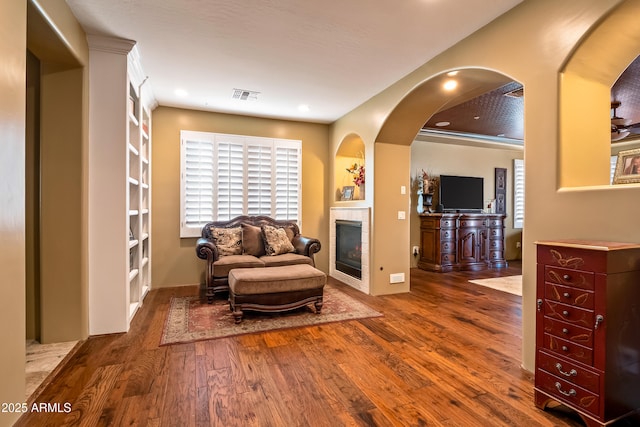 sitting room with a fireplace, visible vents, arched walkways, and wood finished floors