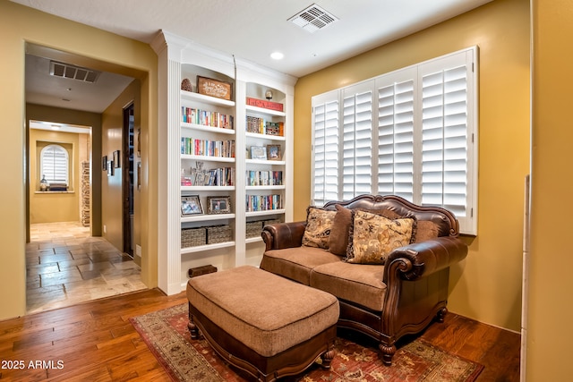 living area with built in shelves, visible vents, and wood finished floors