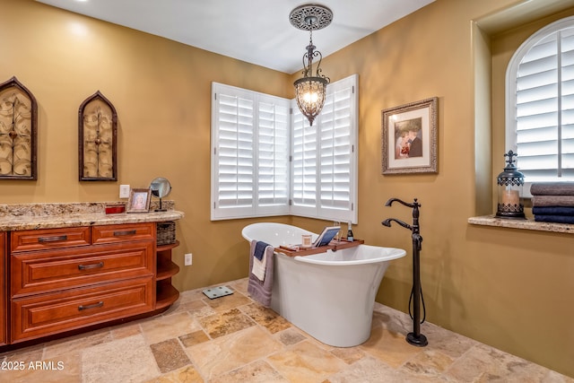 full bathroom with a chandelier, stone tile flooring, a freestanding tub, and vanity