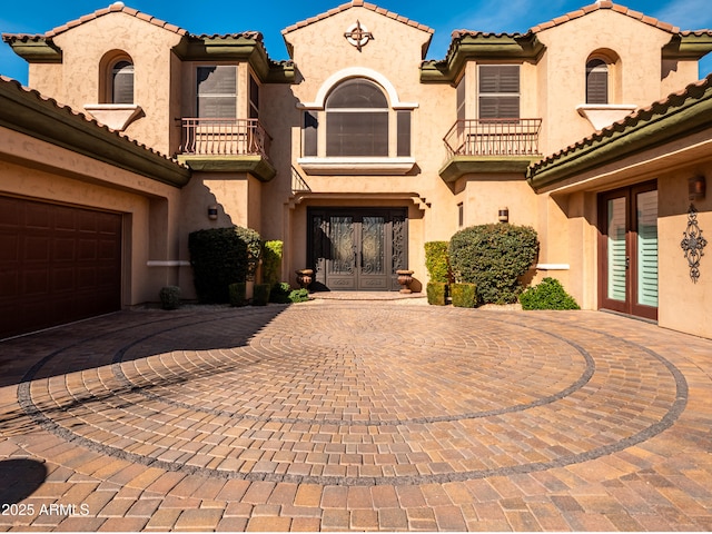 mediterranean / spanish-style house featuring driveway, french doors, a balcony, and stucco siding