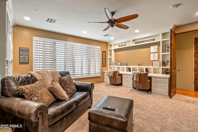 living area featuring ceiling fan, built in desk, light carpet, and visible vents