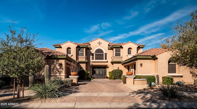 mediterranean / spanish home featuring a balcony, a tiled roof, decorative driveway, and stucco siding