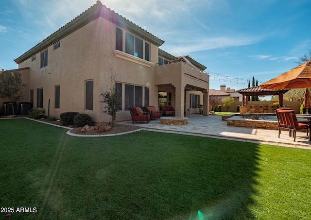 back of property featuring a yard, a patio, stucco siding, a gazebo, and a fire pit