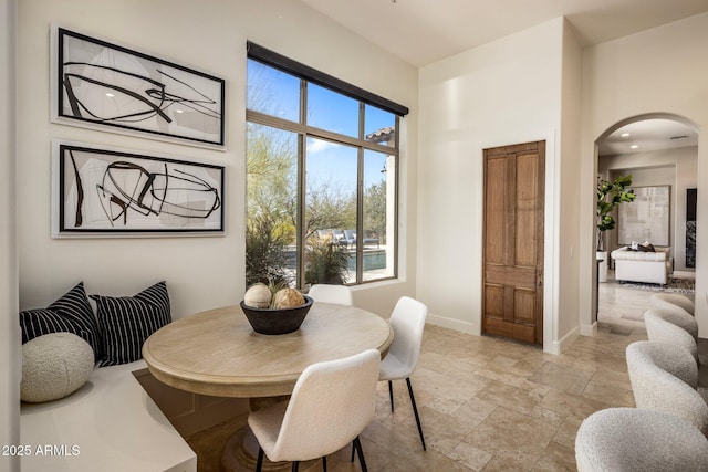 dining space with arched walkways, stone finish flooring, and baseboards