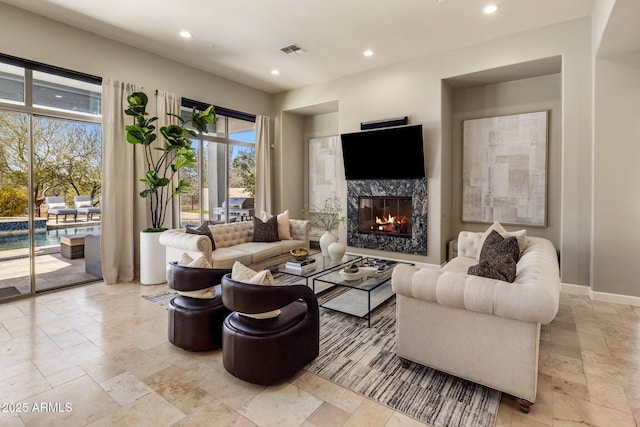 living area with recessed lighting, visible vents, baseboards, stone tile flooring, and a high end fireplace